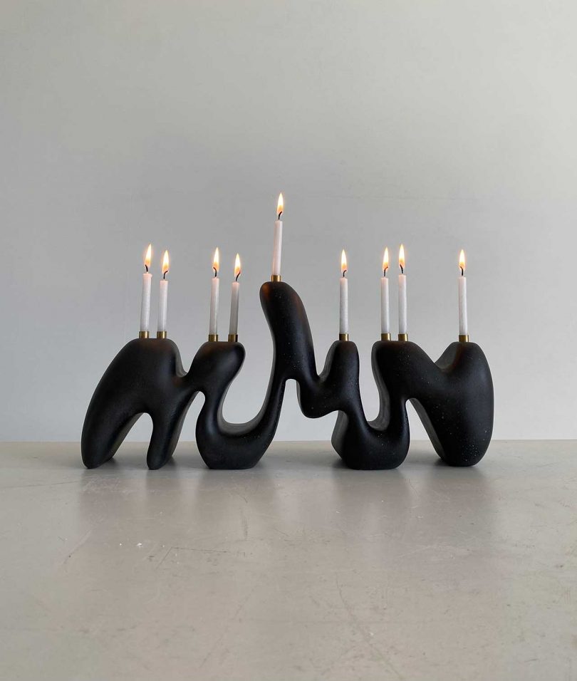 black curvy menorah with white candles lit