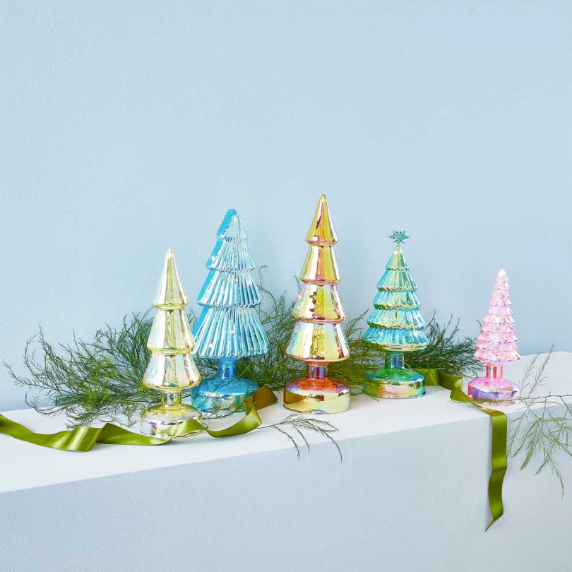 set of 5 iridescent glass trees on a mantel with greenery