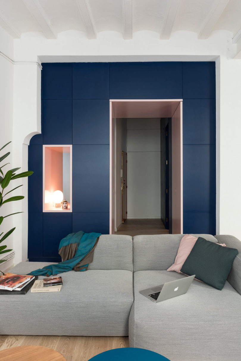partial view in modern apartment of living room with grey sectional sofa with wall of navy cabinets and pink door way