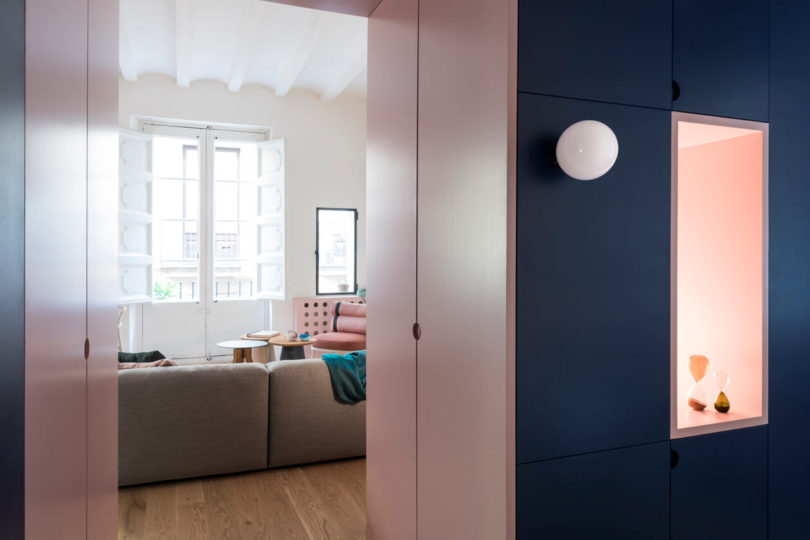 vista do corredor rosa para uma sala de estar moderna com armários marinhos