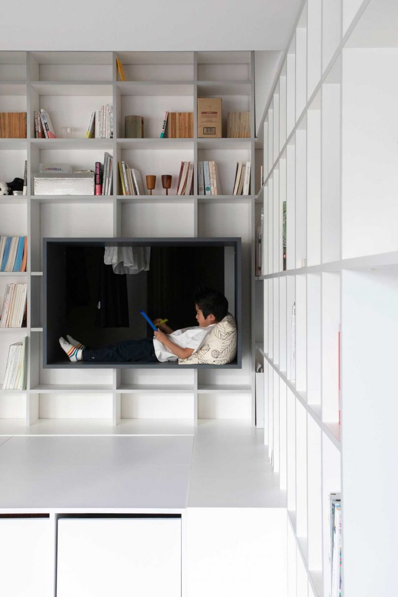 interior shot of modern apartment with floor to ceiling white bookcases with cube with child reading in it