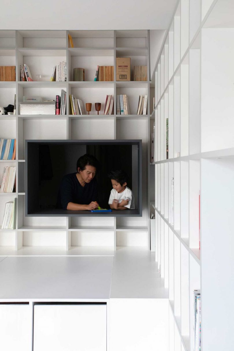 interior shot of modern apartment with floor to ceiling bookcases with cube hosting father and son