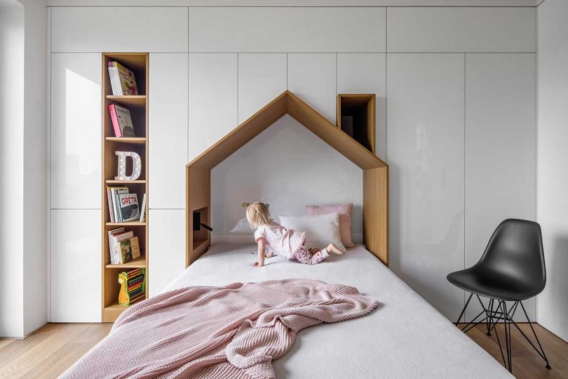 children's bedroom with house-shaped bed embedded into wall of white built-in storage units