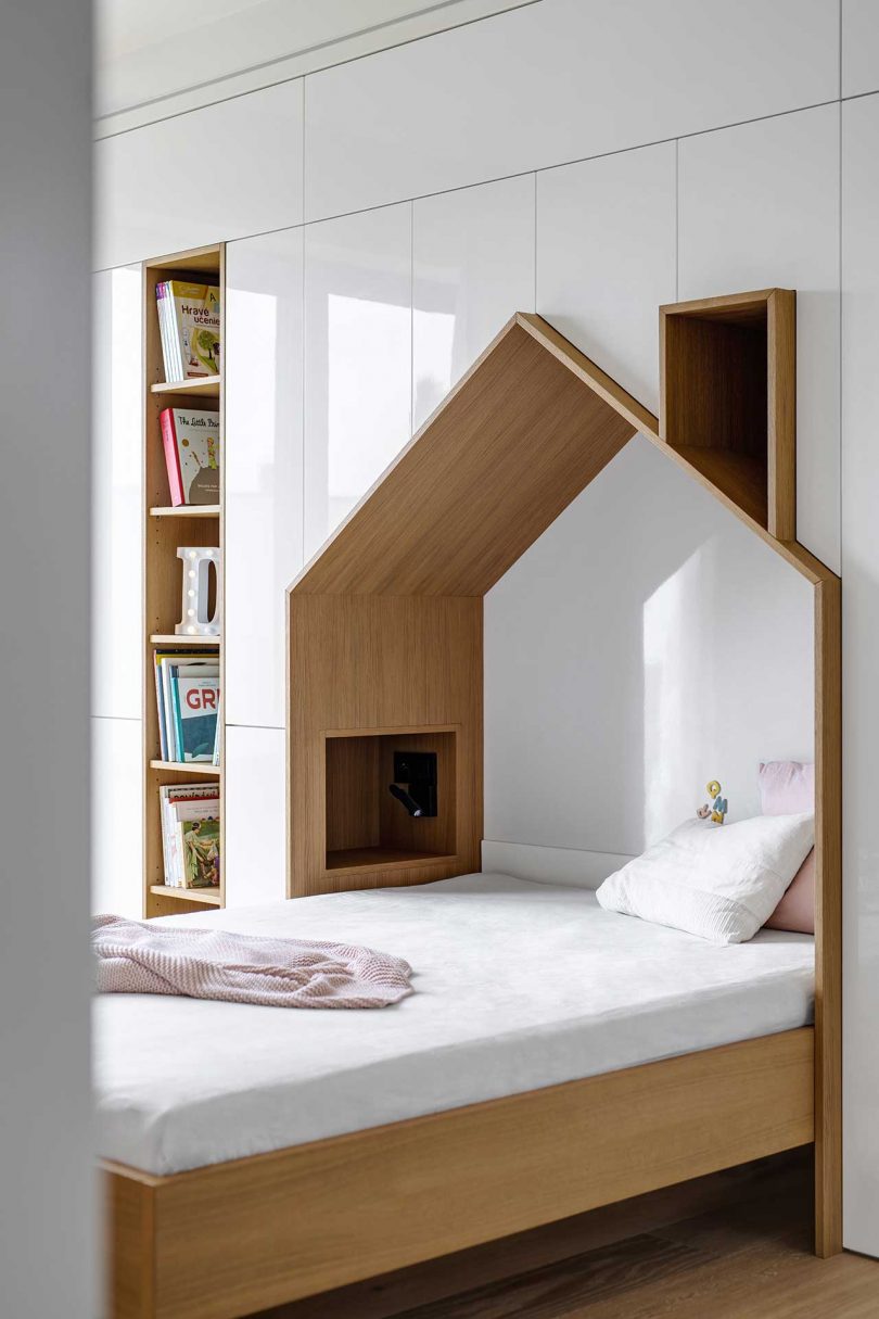 children's bedroom with house-shaped bed embedded into wall of white built-in storage units