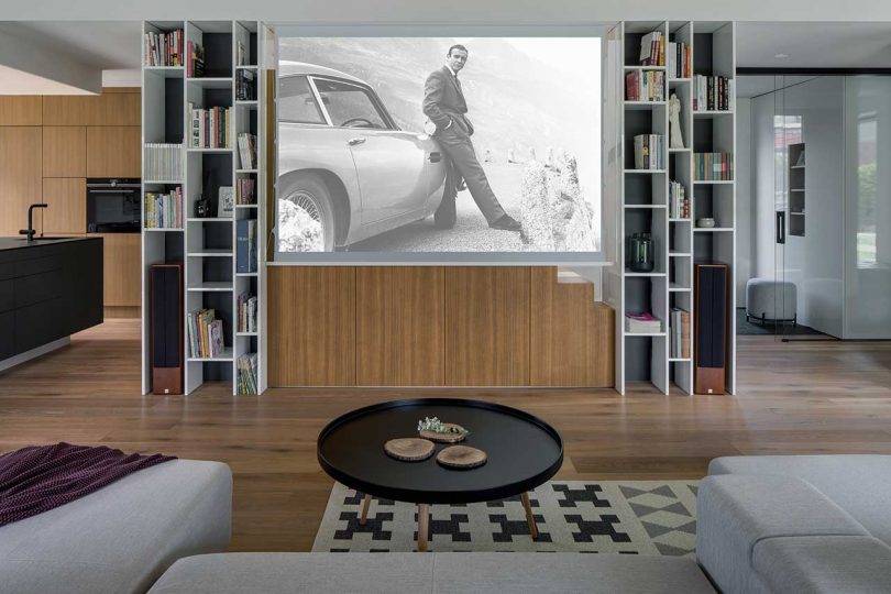 modern living room in concrete, wood, and white surfaces with movie playing on the projector