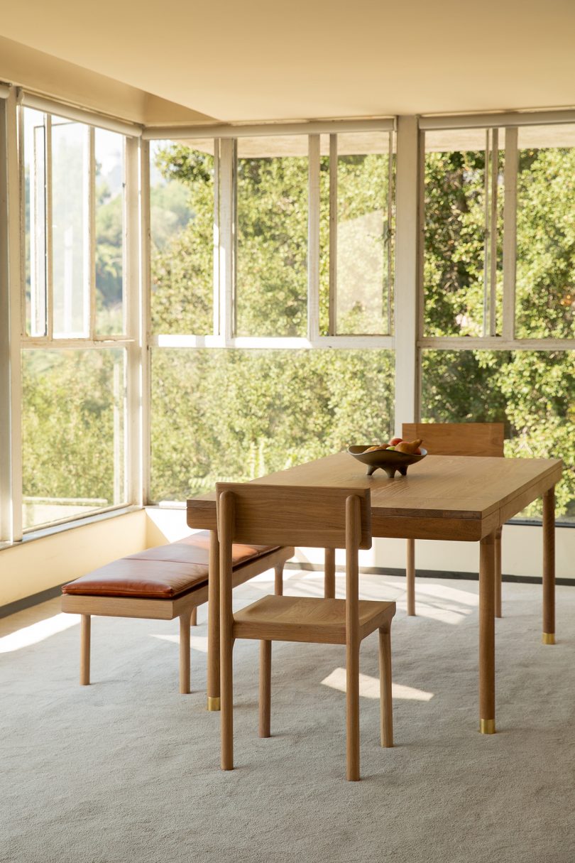 Oak dining table, dining chair, and leather topped bench in window-filled space