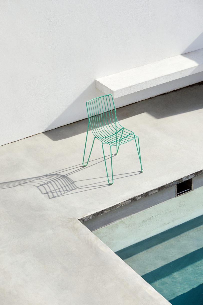 green wire chair sitting poolside next to pool stairs