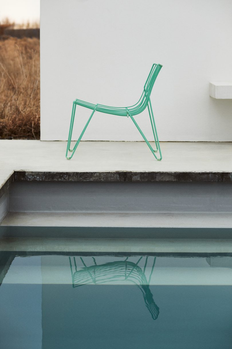 green wire chair sitting poolside next to pool stairs