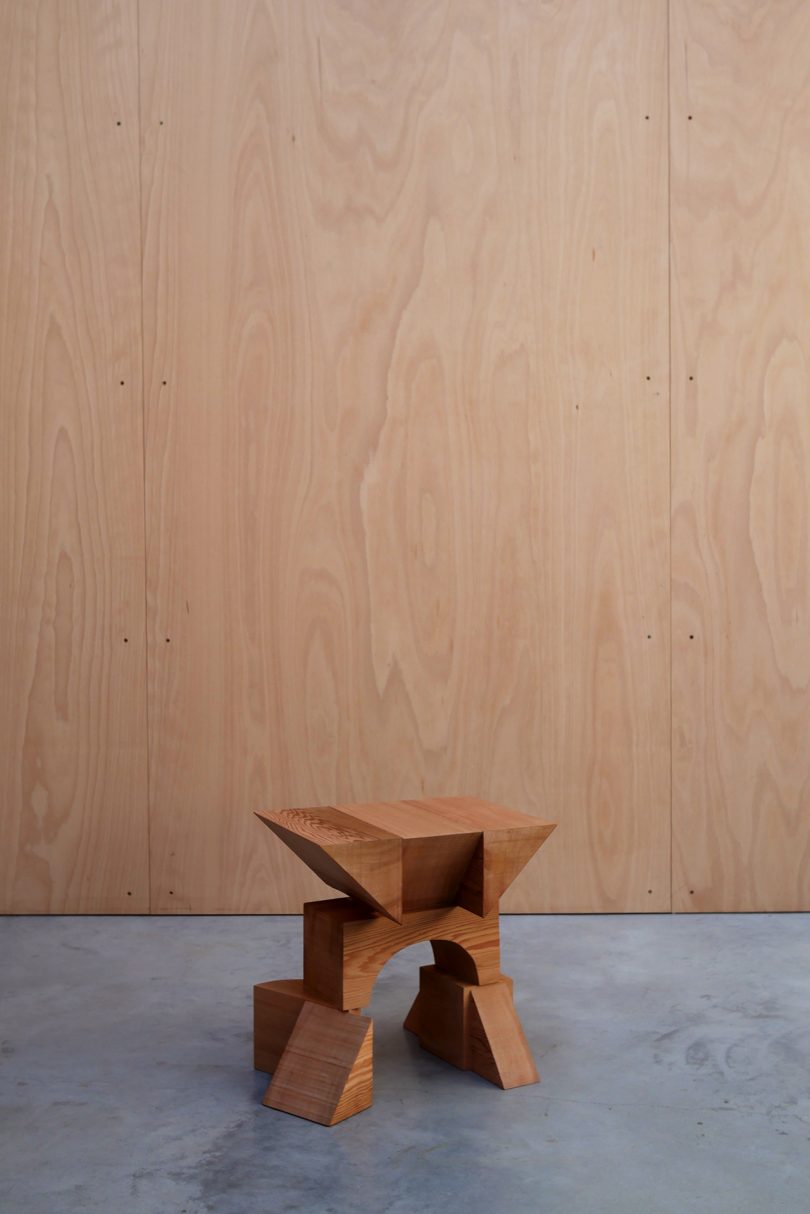 asymmetrical red cedar chair on concrete floor in front of wood wall