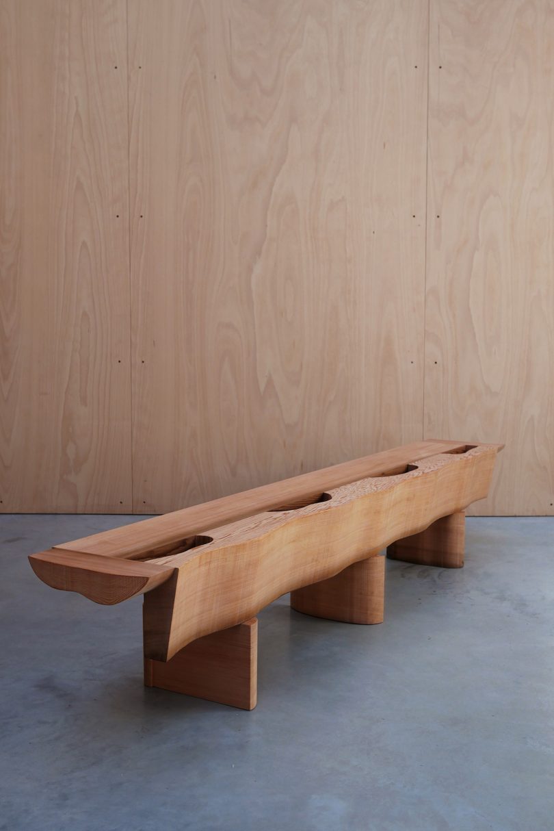 asymmetrical red cedar bench on concrete floor in front of wood wall