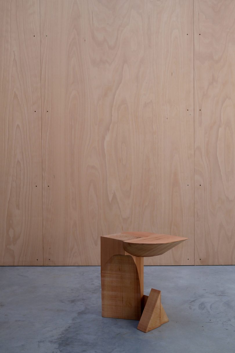 asymmetrical red cedar chair on concrete floor in front of wood wall