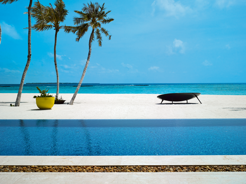 lounge em forma de orbe na praia entre a piscina e o mar com palmeiras e céu azul