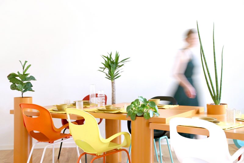orange sculptural table with plants being set for meal