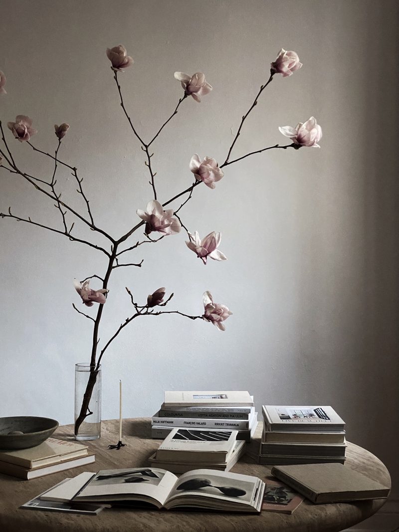 table with large vase, branch, and book stacks