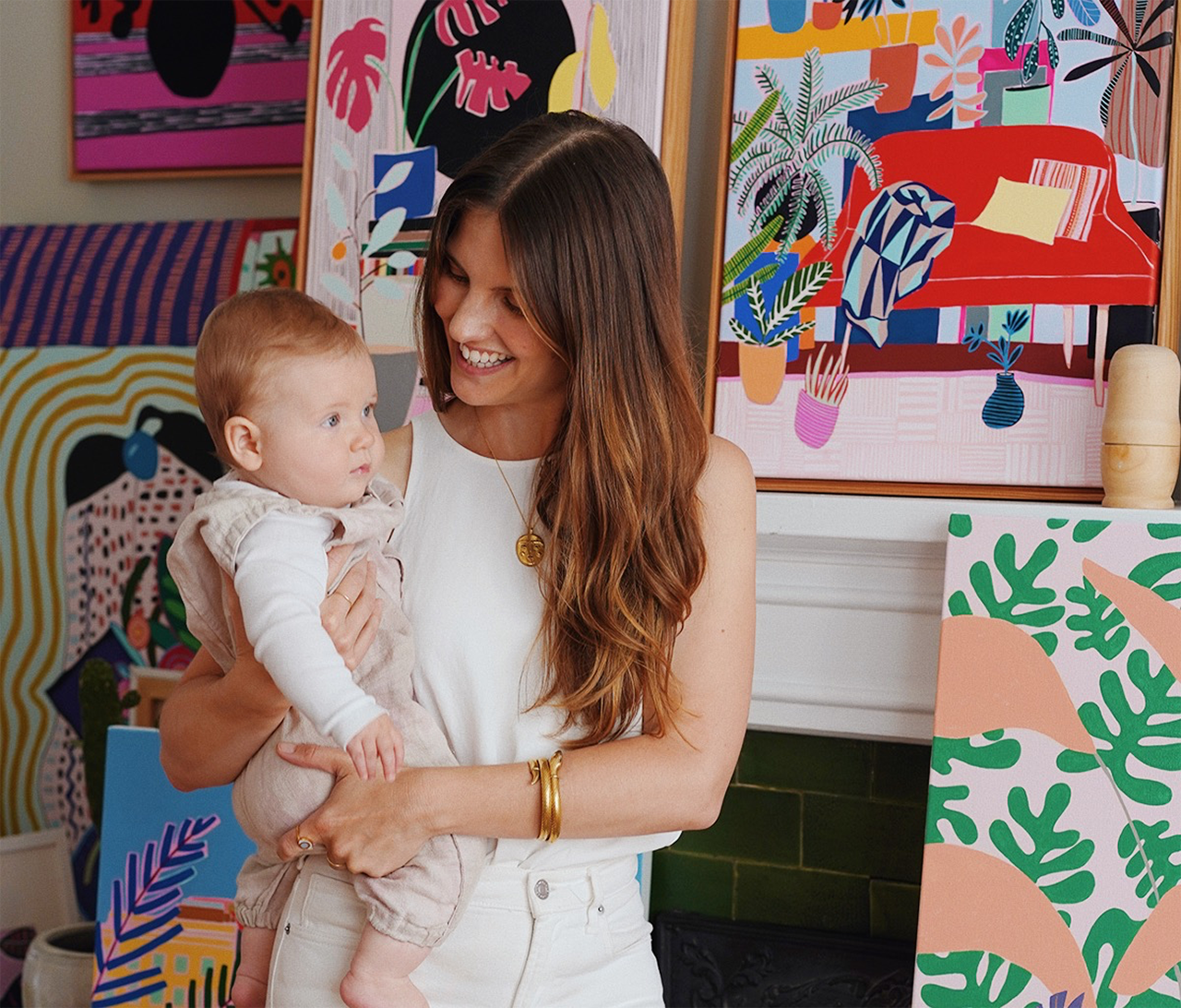 light skinned woman holding child standing in front of artworks