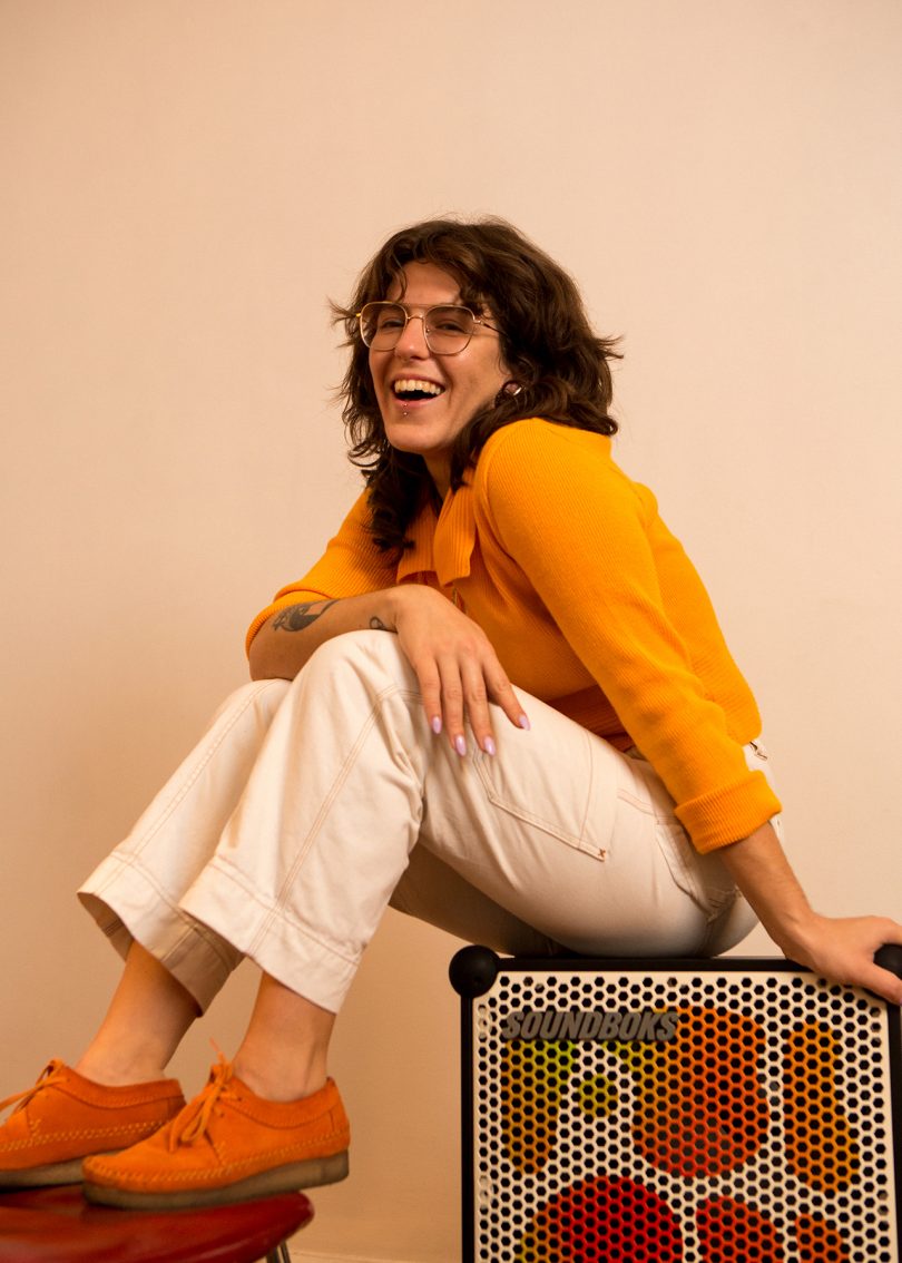 light skinned woman with dark hair and glasses sitting on box and smiling