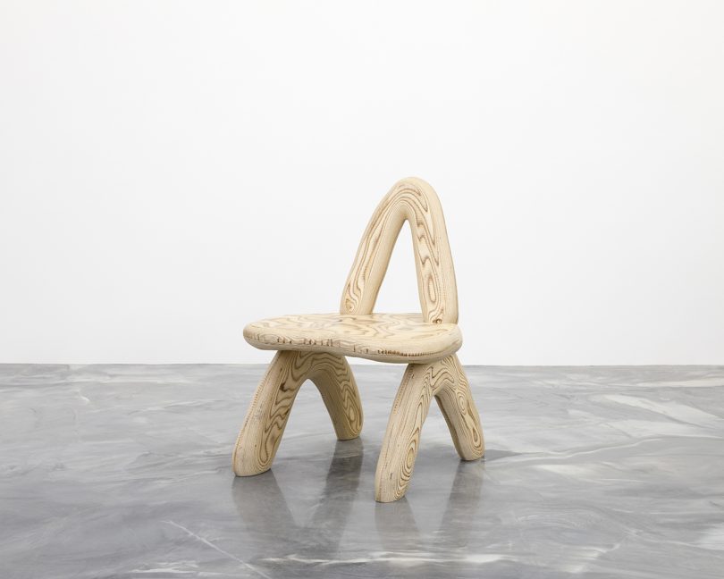 curvaceous wooden chair on concrete floor in front of white wall