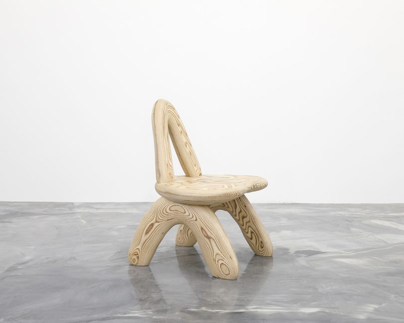 curvaceous wooden chair on concrete floor in front of white wall