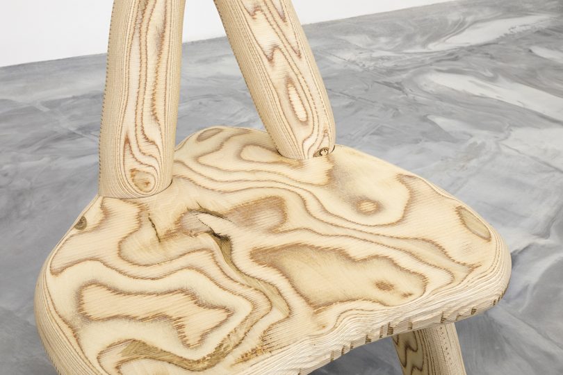 detail of curvaceous wooden chair on concrete floor in front of white wall