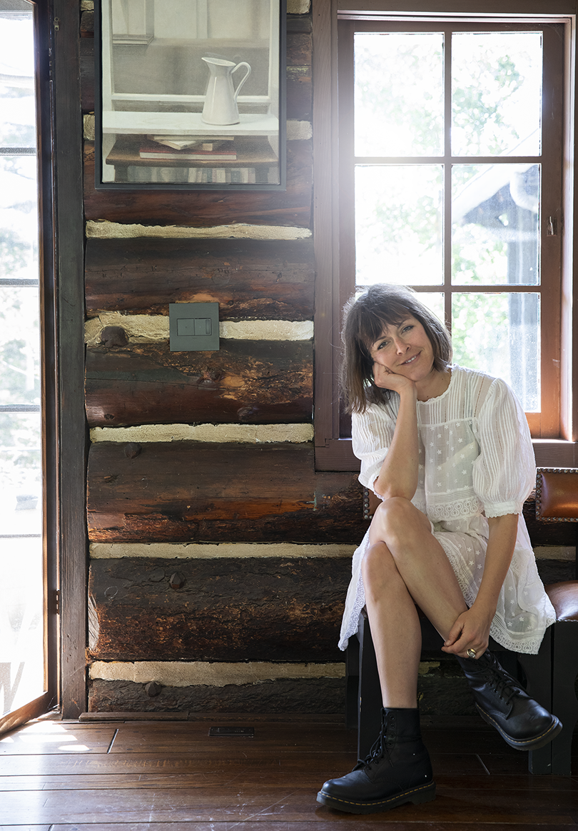 light-skinned woman wearing a white dress and boots sitting on a bench against an interior wall