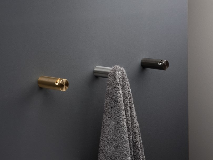 three modern towel hooks mounted to black wall with towel