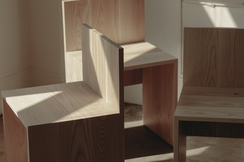 three primitive wood chairs on concrete floor in front of white wall