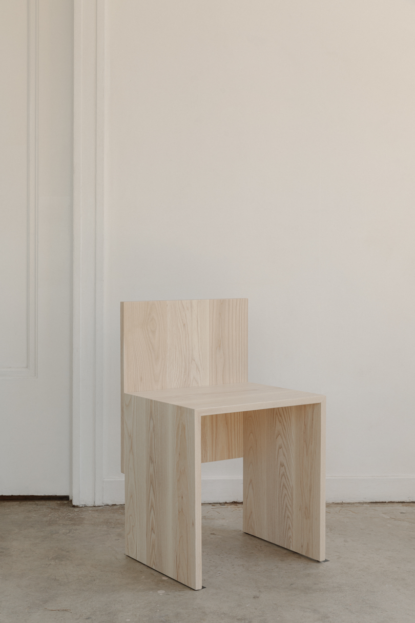 primitive wood chair on concrete floor in front of white wall