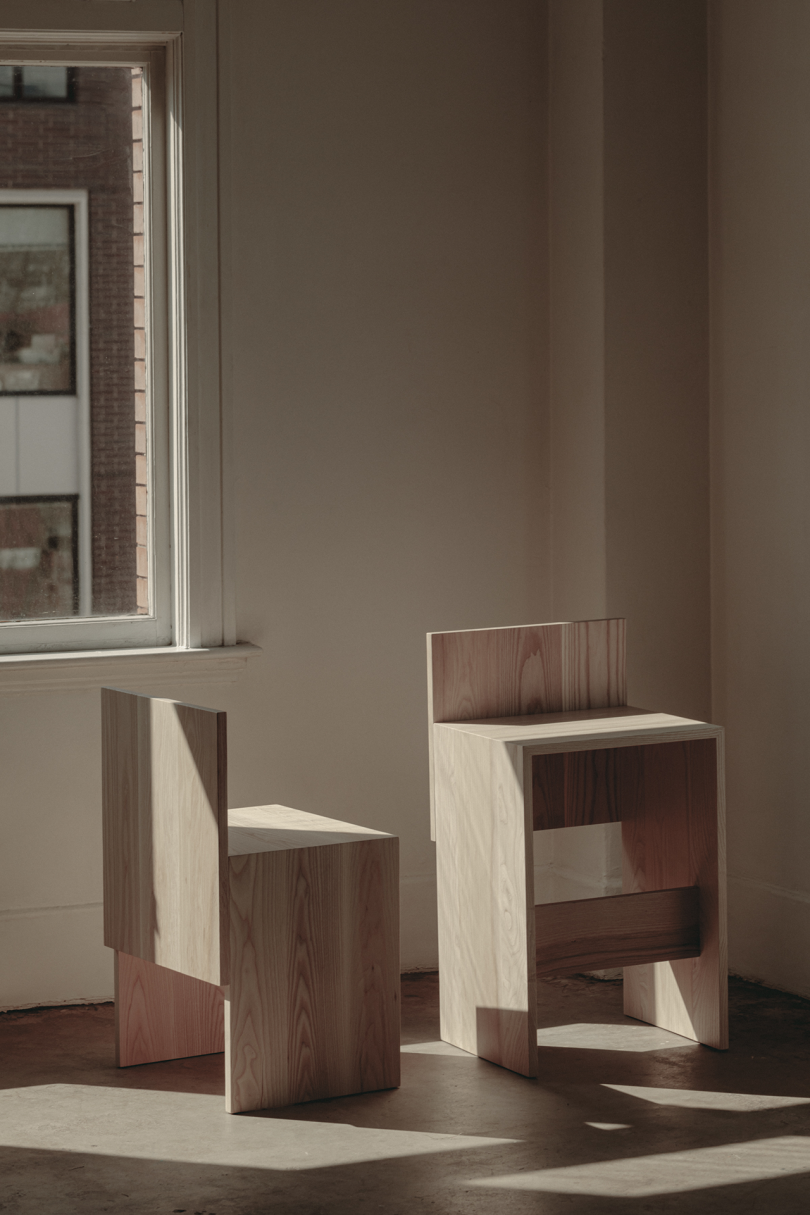 two primitive wood chairs on concrete floor in front of white wall