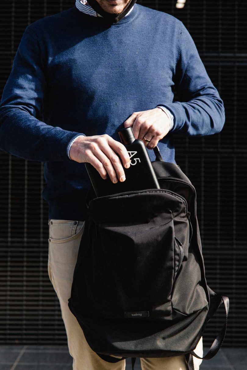 man placing flat black water bottle in backpack