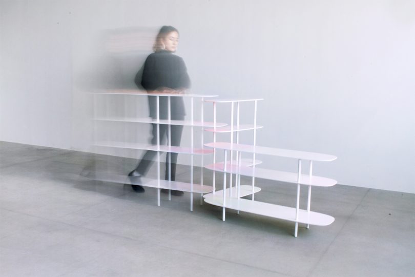 white shelves on a concrete floor and in front of a white wall with a blurred person walking behind them