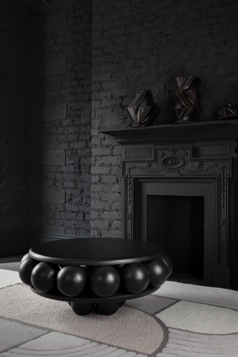 bulbous black coffee table sitting in front of a dark colored fireplace and wall