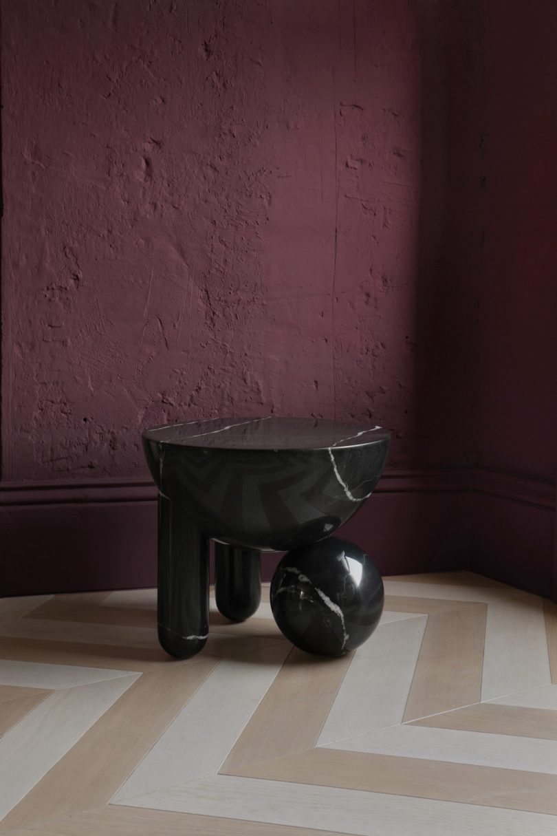 dark geometric small table in front of a mulberry colored wall