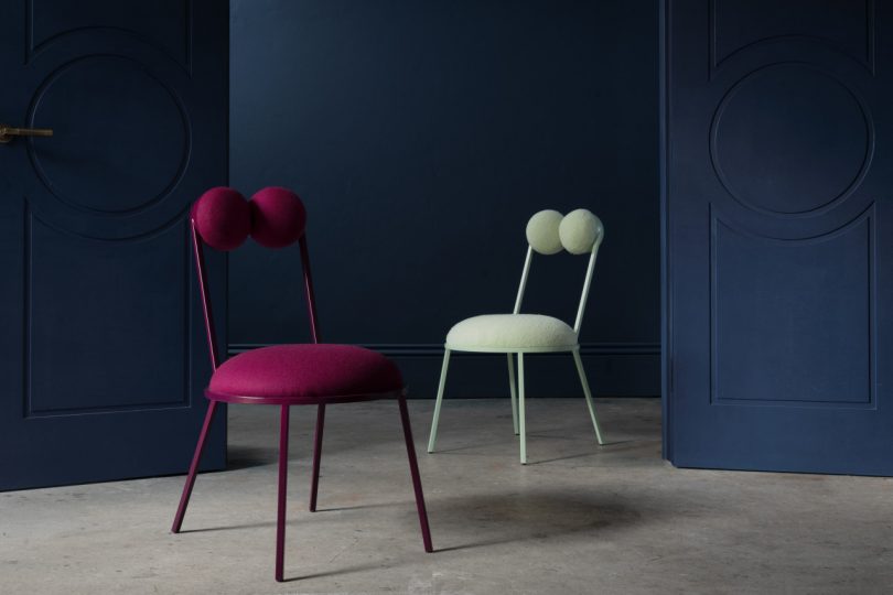 one berry and one white geometric dining chair in front of dark wall