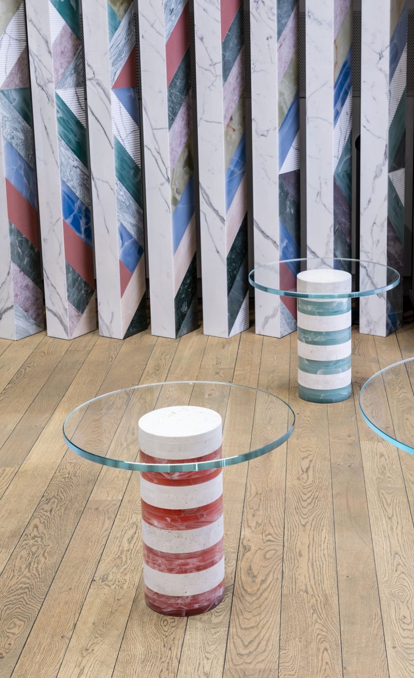 two striped tables with round glass tops in front of mural