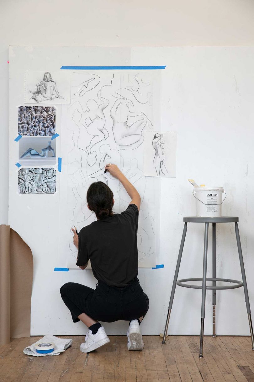 artist squatting down and sketching abstract pattern on wall