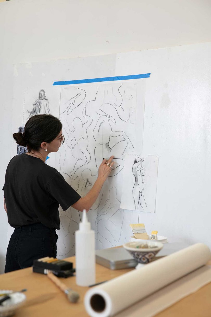 artist sketching on paper taped to a wall