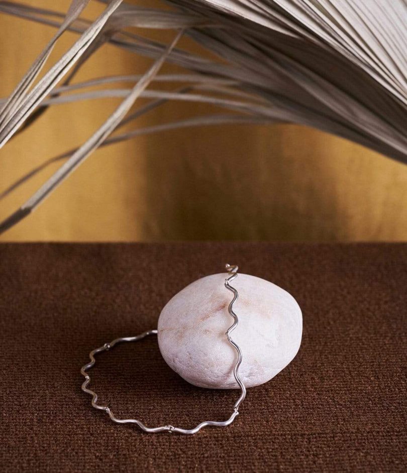 silver necklace draped over a white rock with brown background