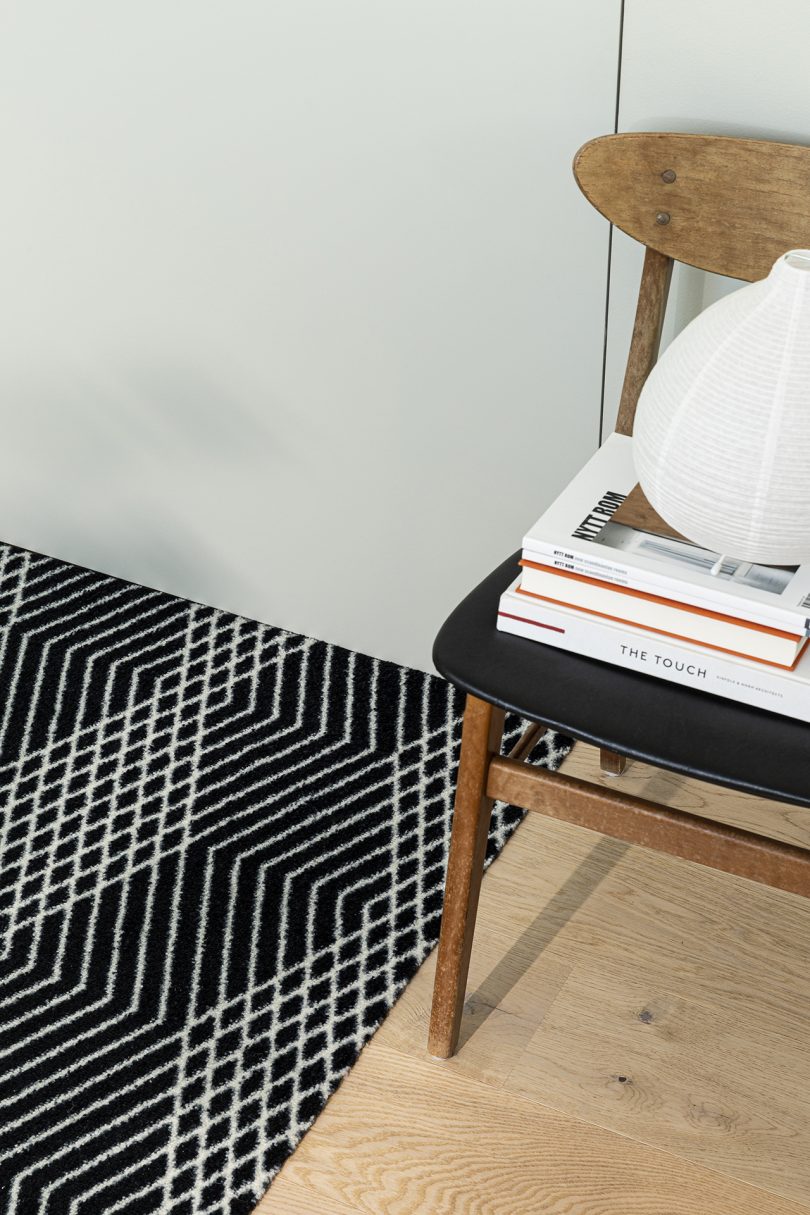 black and white patterned door mat detail with chair stacked with books on right