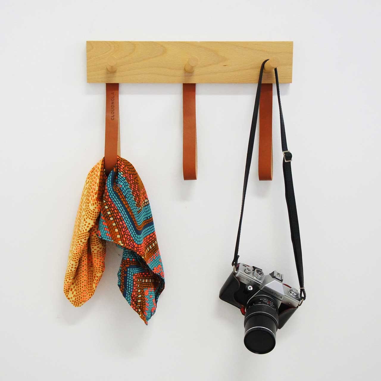 wall-mounted wooden coat rack with leather straps holding a scarf and camera