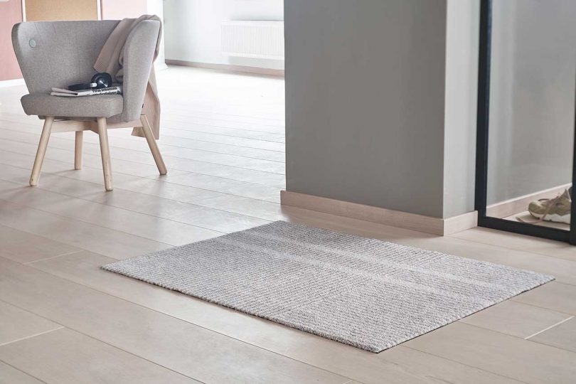 beige and white mat laying on pale wood floor with gray wall and window