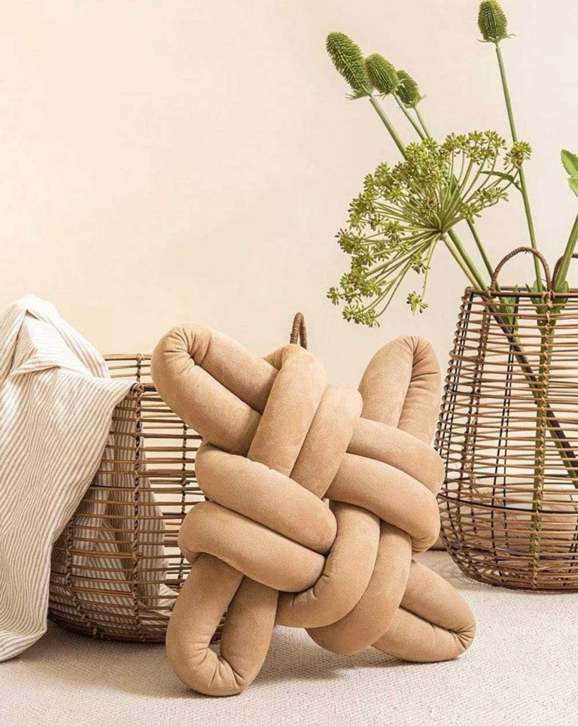 beige knot pillow resting in front of two baskets