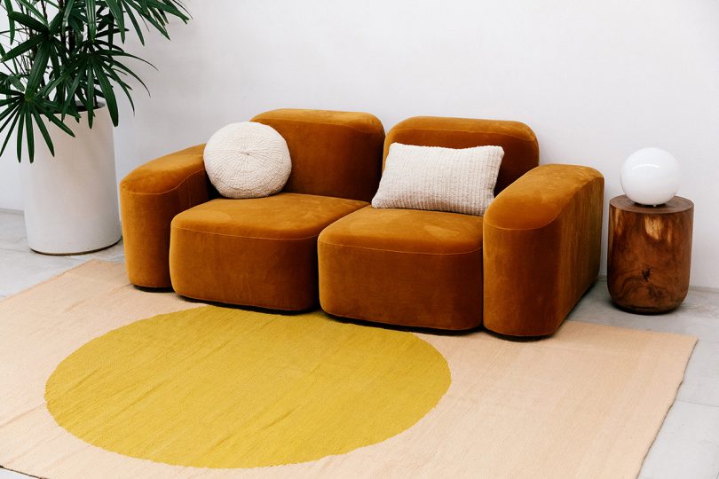 rust colored couch with two white pillows and large woven floor rug