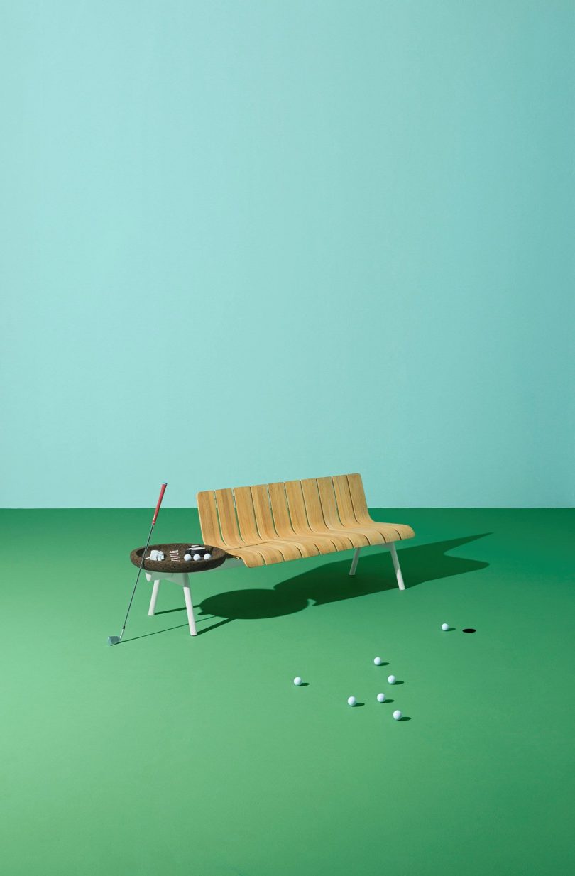 wood and aluminum outdoor bench and table on green floor in front of light blue wall