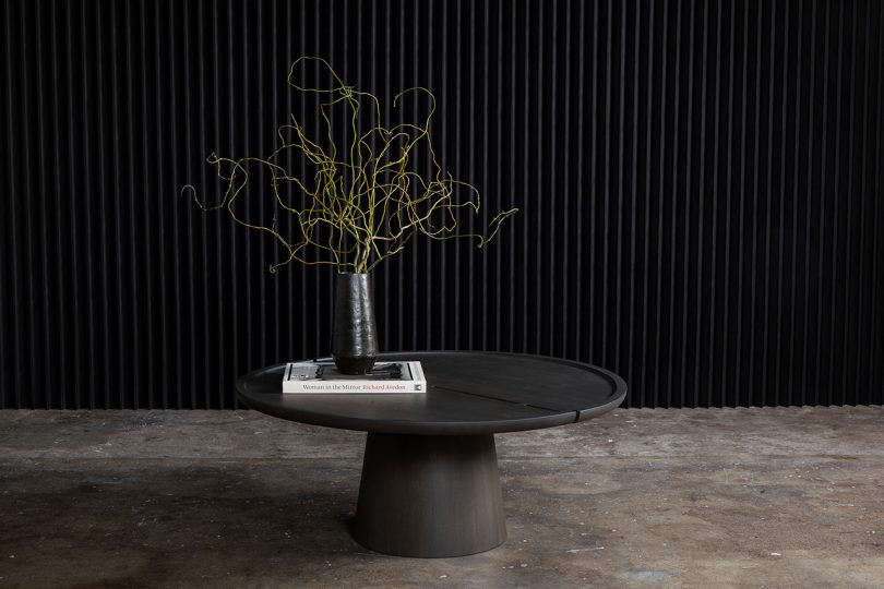 round pedestal table styled with book and vase of flowers on cement floor with black background