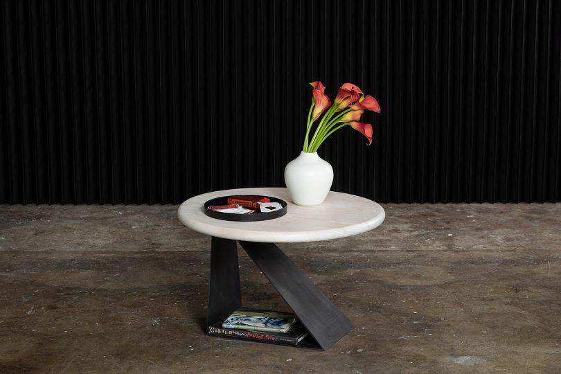 round side table styled with tray and vase of flowers on cement floor with black background
