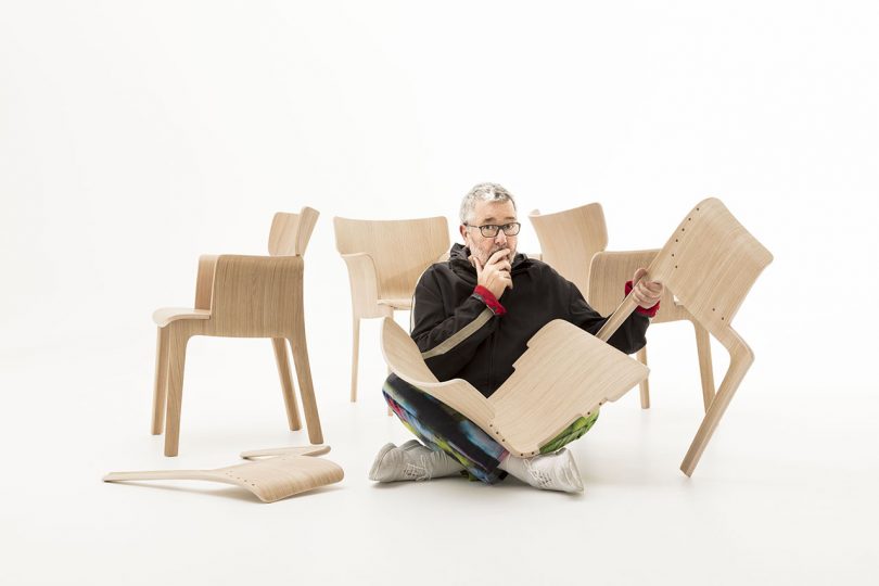 light skinned man with white hair and glasses examines a wood chair