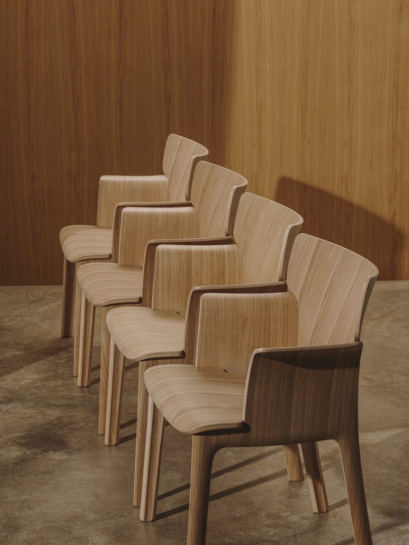 four wood armchairs lined up in front of wood paneled wall