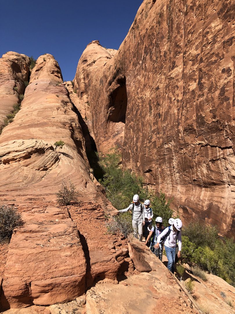 five people in a line walking through a canyon
