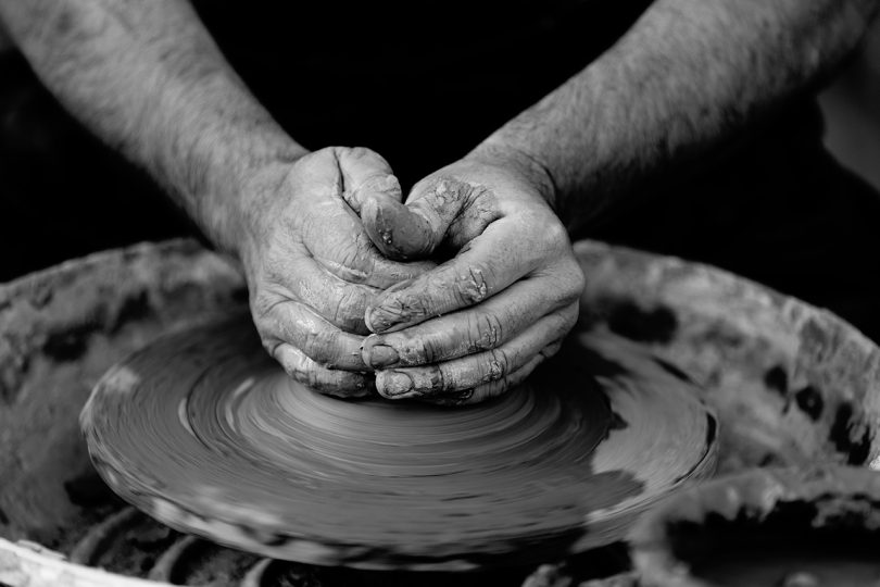 black and white image of two hands using a clay throwing wheel