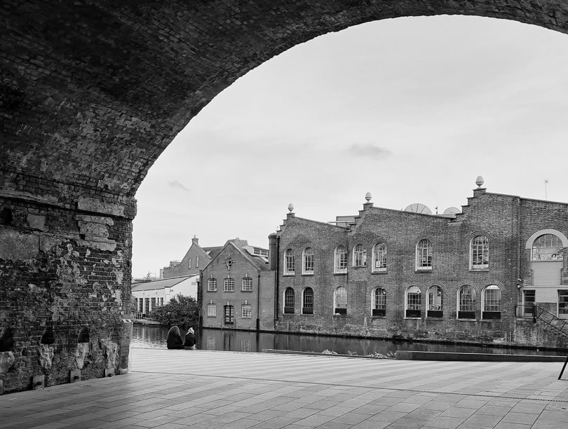 black and white image of building viewed through large stone archway